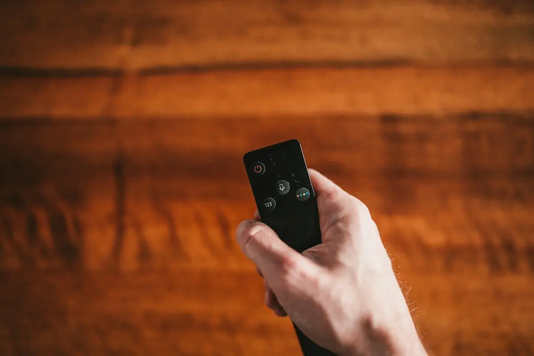 Une main tient une télécommande devant un mur en bois, au moment de choisir une IPTV en France comme Premier IPTV