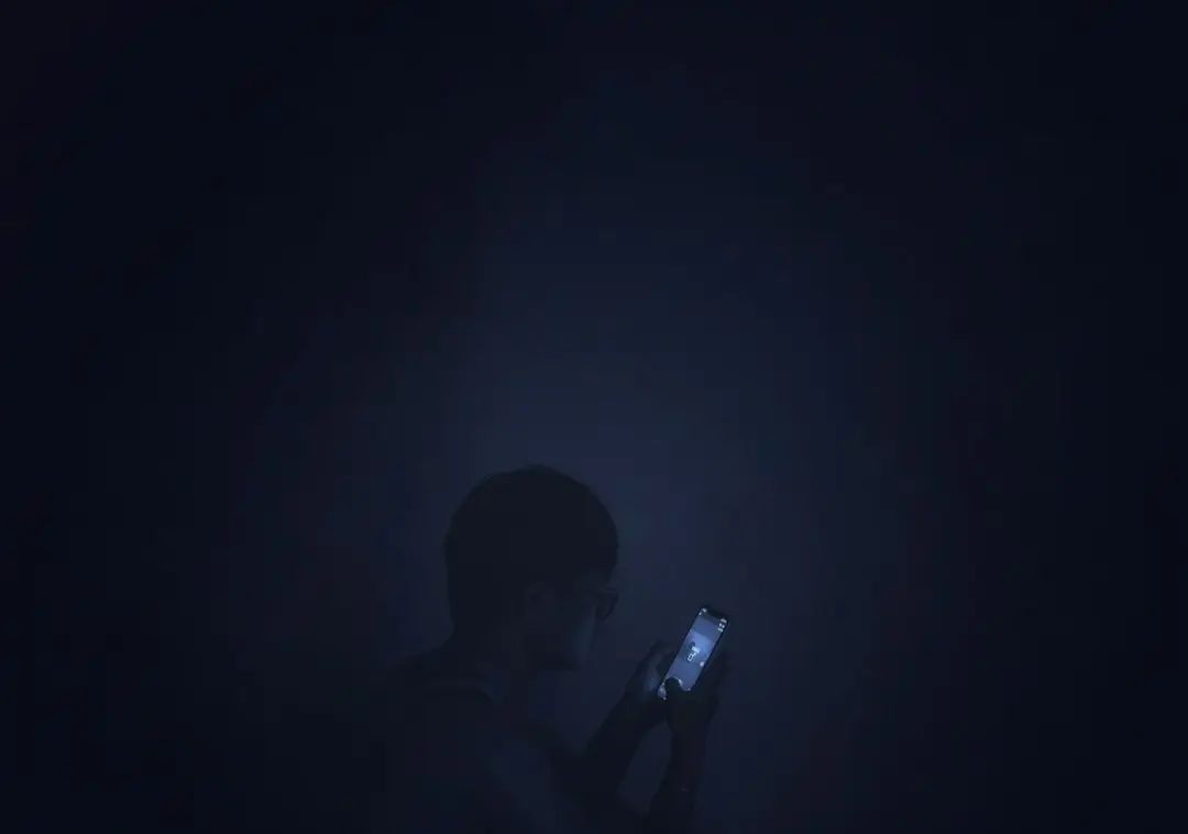 Une personne éclaire son visage avec son smartphone dans une pièce baignée de bleu, pour configurer IBO Player Pro avec Premier IPTV